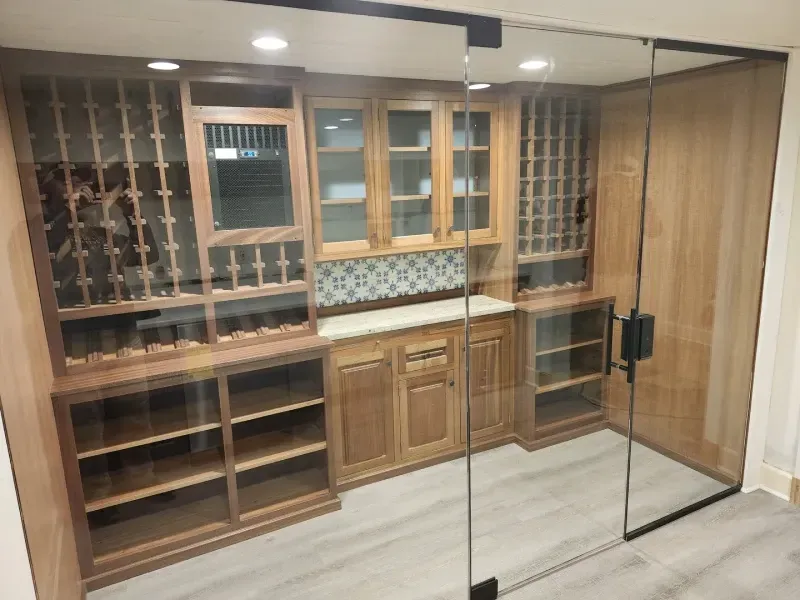 Wine cellar with wood cabinetry, glass door, and tiled backsplash.