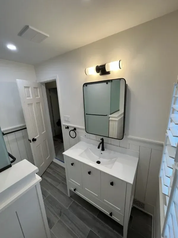 Bathroom with white vanity, black faucet, and rectangular mirror. White walls with dark trim.