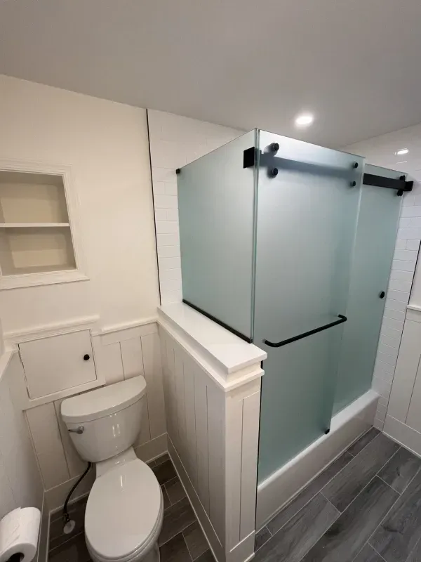 Bathroom with a frosted glass shower, toilet, and white wainscoting. Dark gray tiled floor.