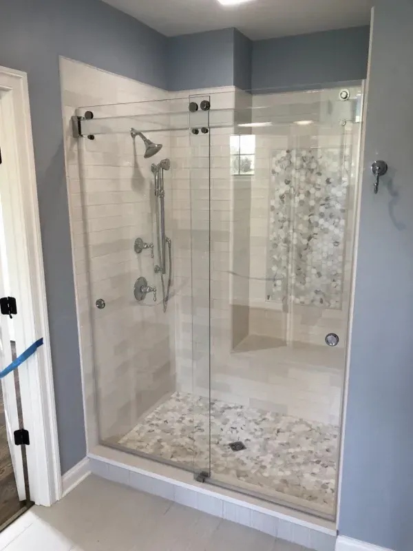 Glass shower enclosure with white tile and pebble floor, inside a bathroom with blue walls.