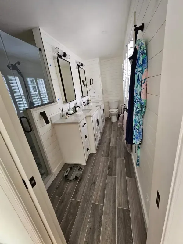Bathroom with white cabinets, dark mirrors, shower, and patterned robe. Gray wood-look tile floor.