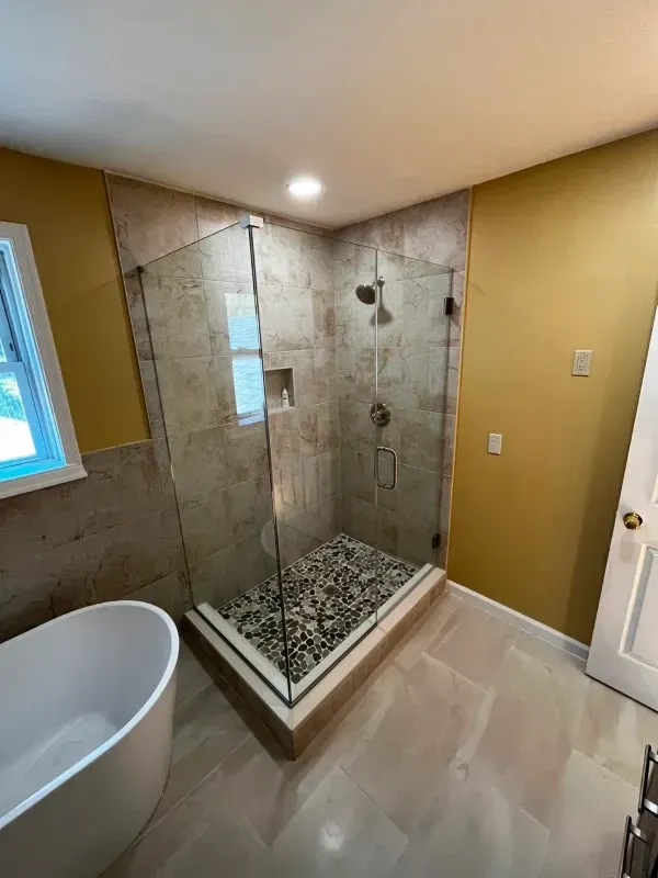 Modern bathroom with a glass shower, stone tile, and gold walls.