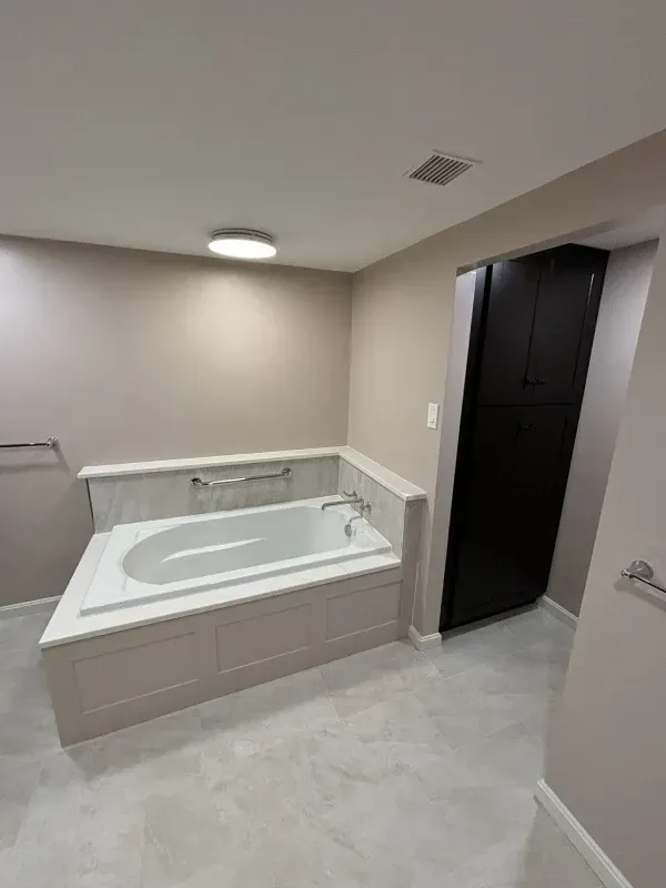 Bathroom with a built-in white bathtub, tan walls, and a dark storage cabinet.