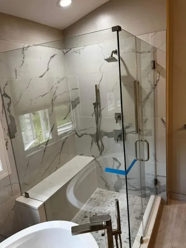 Modern bathroom with glass shower enclosure, marble-look tile, and freestanding tub.