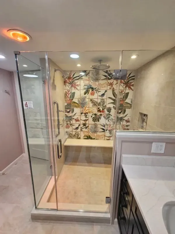A modern bathroom with a glass shower enclosure featuring floral tile, a bench, and a rainfall showerhead.