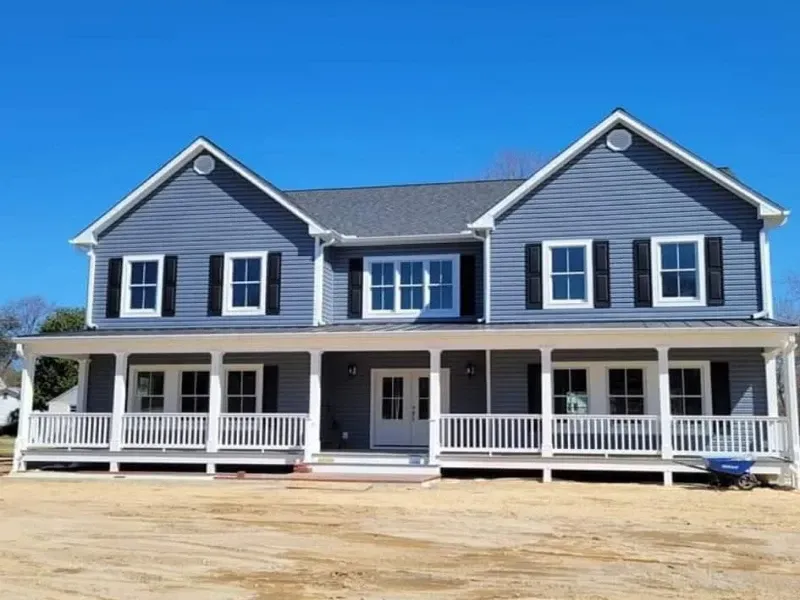 Two-story blue house with white trim, porch, and black shutters under a clear sky.