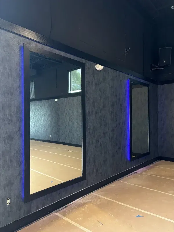 Room with two large rectangular mirrors on a dark textured wall; blue lighting accents the mirror frames.