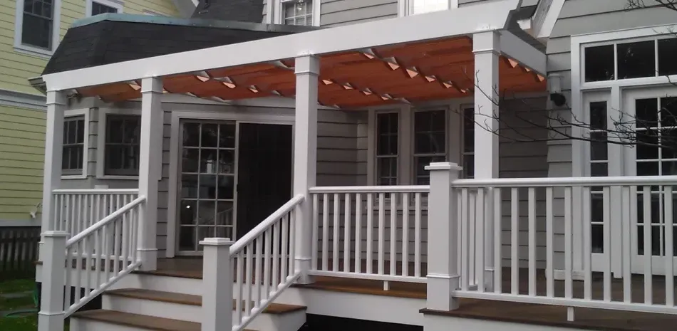 White porch with steps, railings, and overhead canopy, leading to a house with windows and a door.