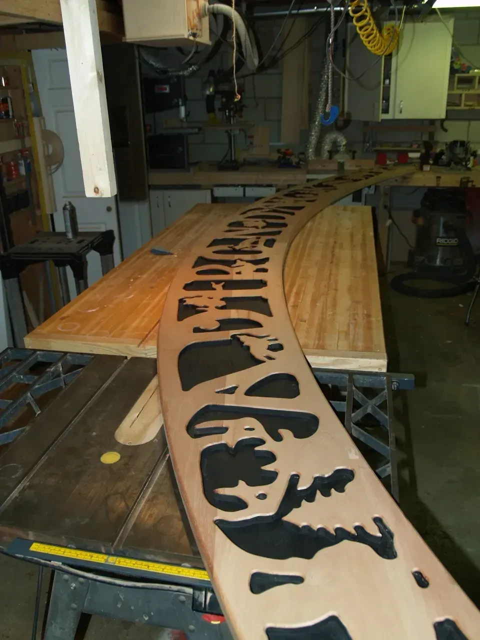 Wooden board with intricate cut-out design being worked on by a CNC machine in a workshop.