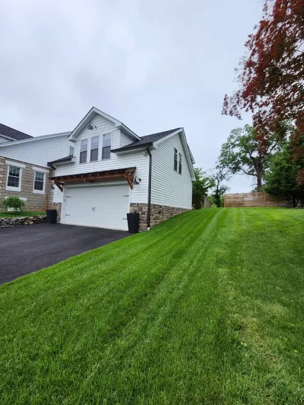 White house with a garage door and green lawn, stone foundation. Overcast sky.