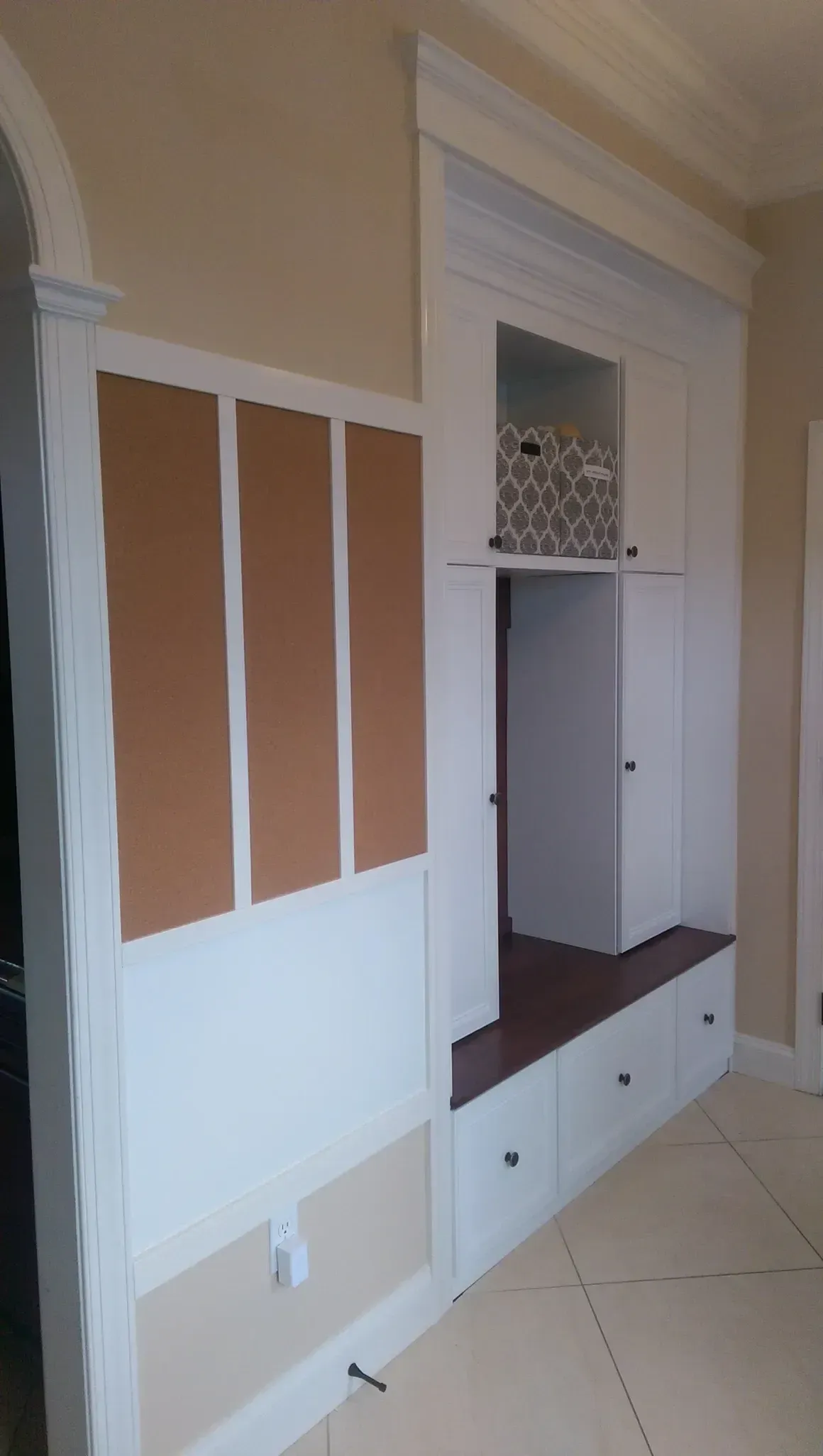 Built-in white storage unit with bulletin boards, bench, drawers, and cabinet in a hallway.
