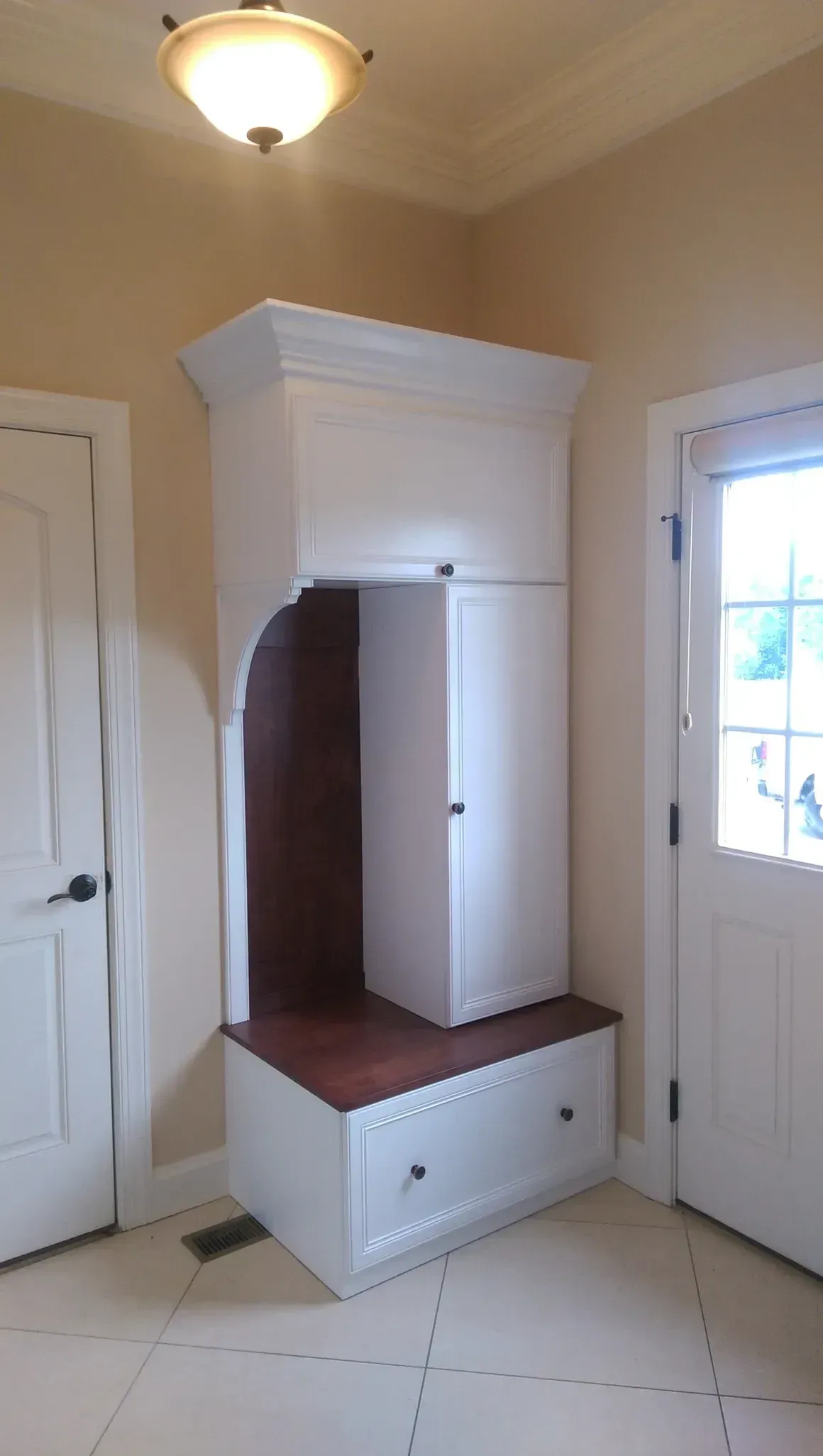 White built-in entryway storage unit with bench, cabinets, and a dark wood-toned niche.
