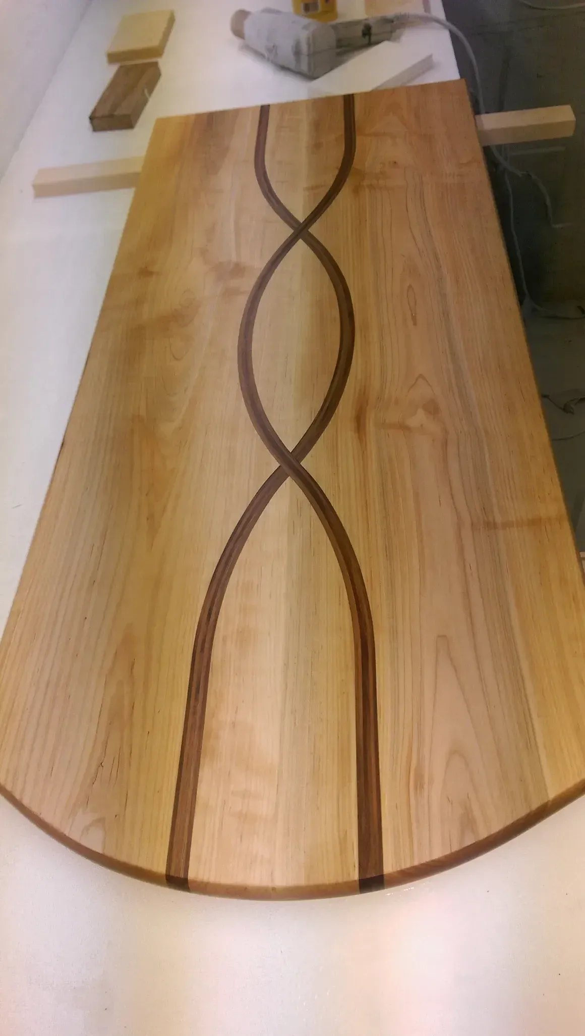 Wooden table with a dark brown, figure-eight inlay. Curved edges, light wood grain.