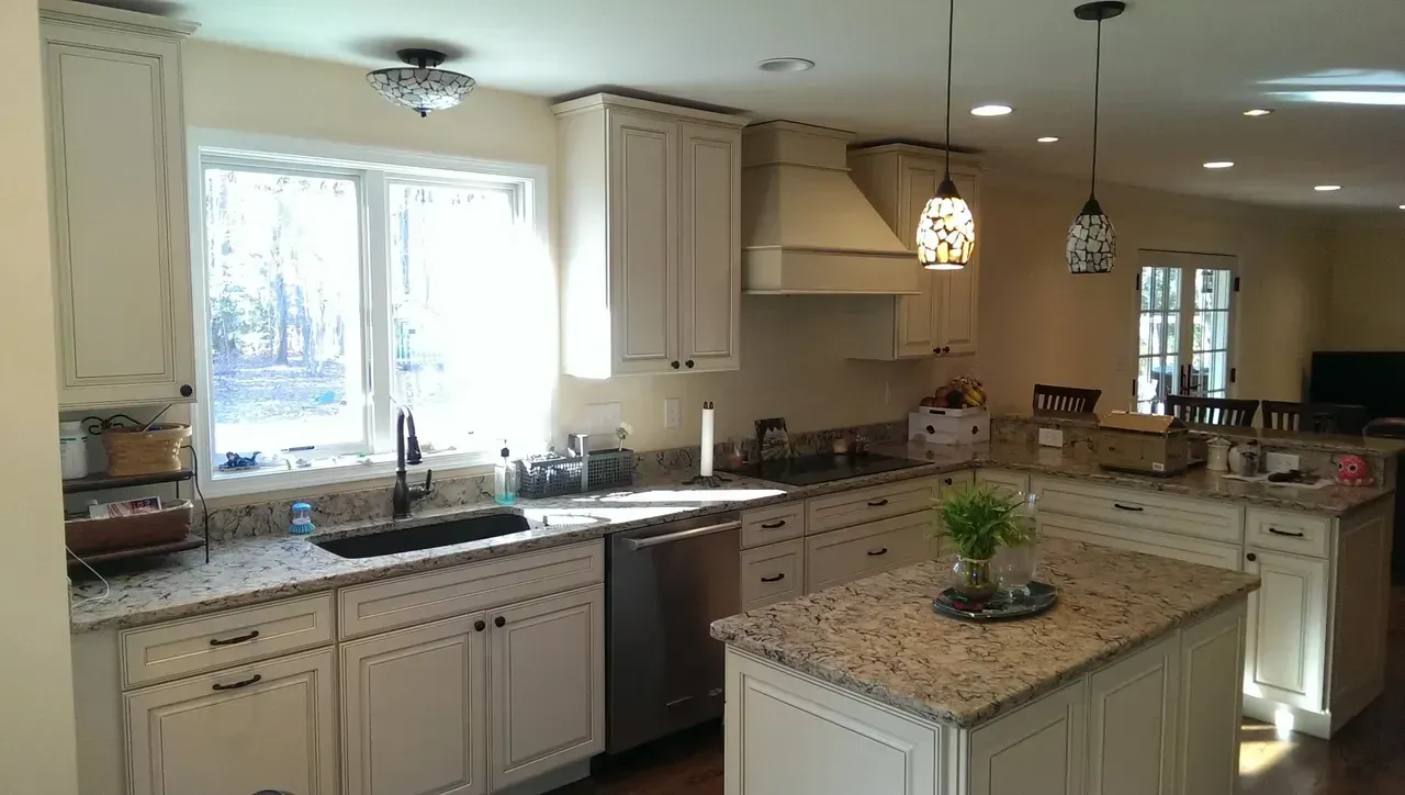 Cream-colored kitchen with granite countertops, stainless steel appliances, and an island. Bright sunlight streams through the window.