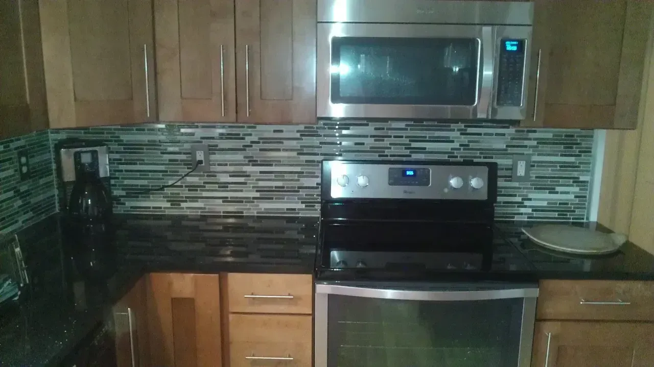 Kitchen with a microwave above an oven, brown cabinets, and a mosaic tile backsplash.