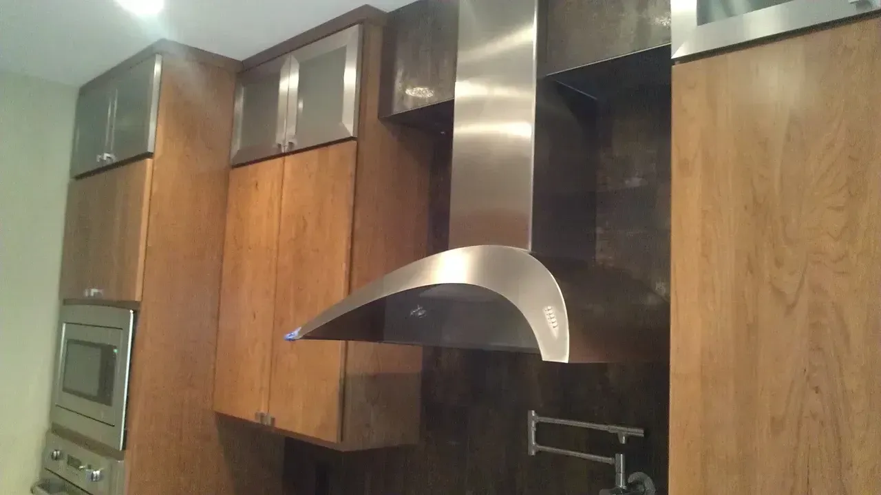 Kitchen with stainless steel range hood, wooden cabinets, and a microwave oven.