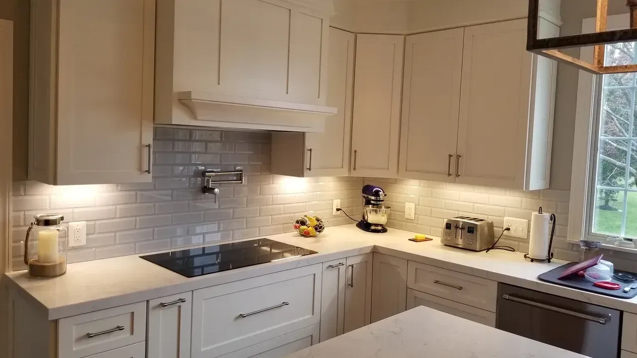 Kitchen with off-white cabinets, white backsplash, cooktop, and pot filler. Countertops and appliances visible.