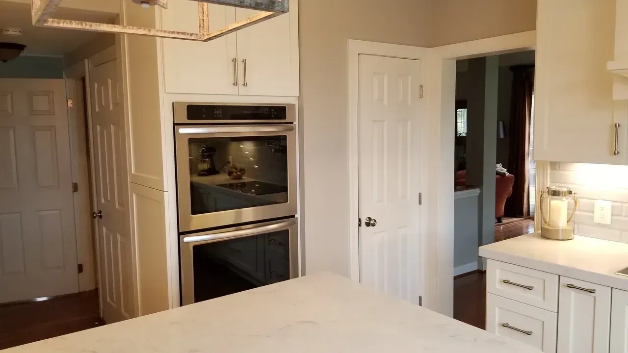 Kitchen with white cabinets, stainless steel oven, and island. Doorways lead to other rooms.
