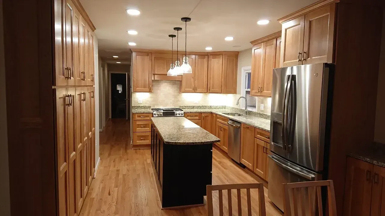Kitchen with light wood cabinets, granite countertops, stainless steel appliances, and a black island.