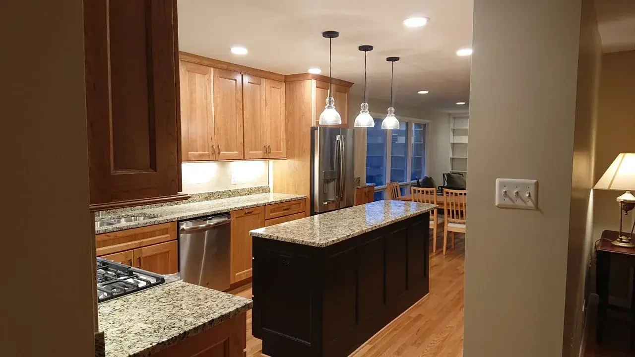 Kitchen with light wood cabinets, dark island, stainless steel appliances, and granite countertops.