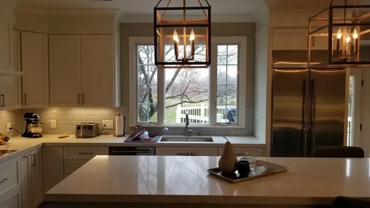 Kitchen with white cabinets, stainless steel appliances, large window, and island with lighting.