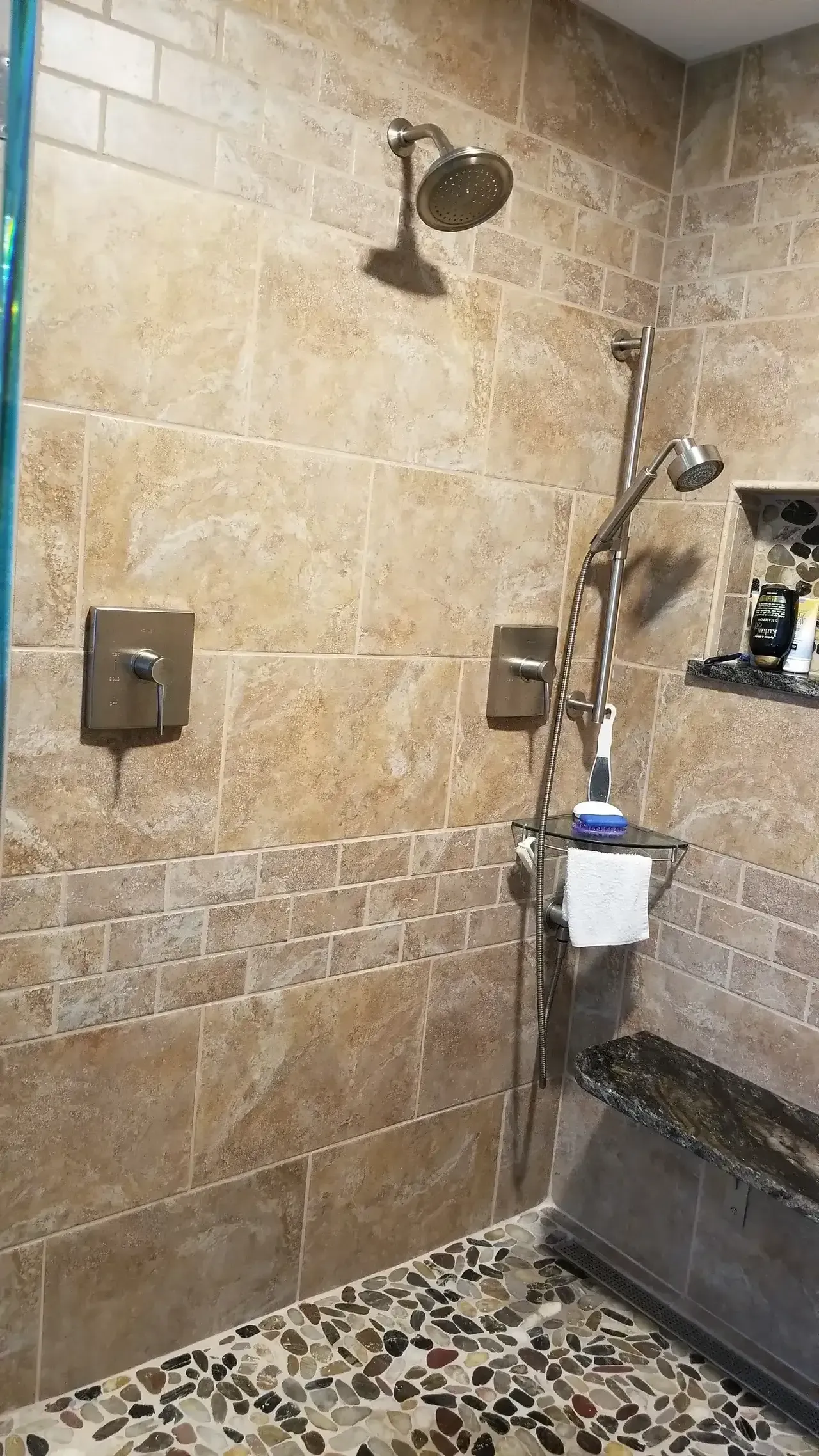 Shower with beige tile, pebble floor, and multiple showerheads. Includes a built-in bench.