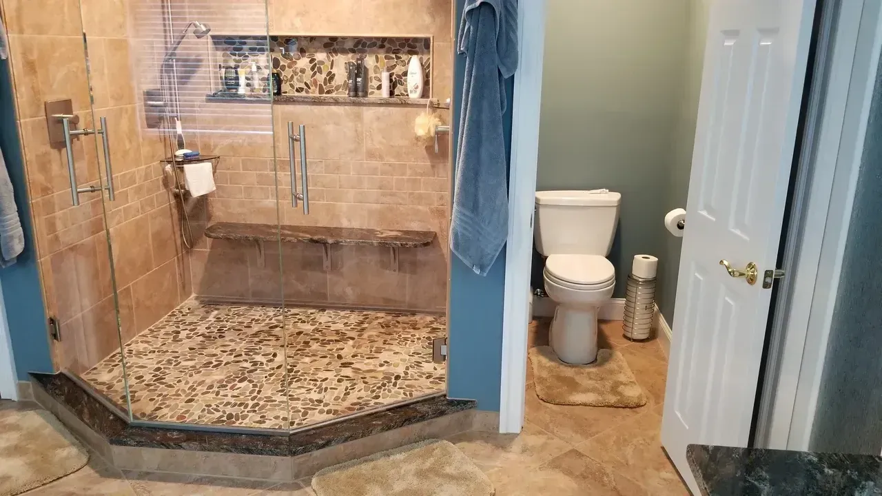 Bathroom with tiled shower, pebble floor, glass door, and toilet visible.