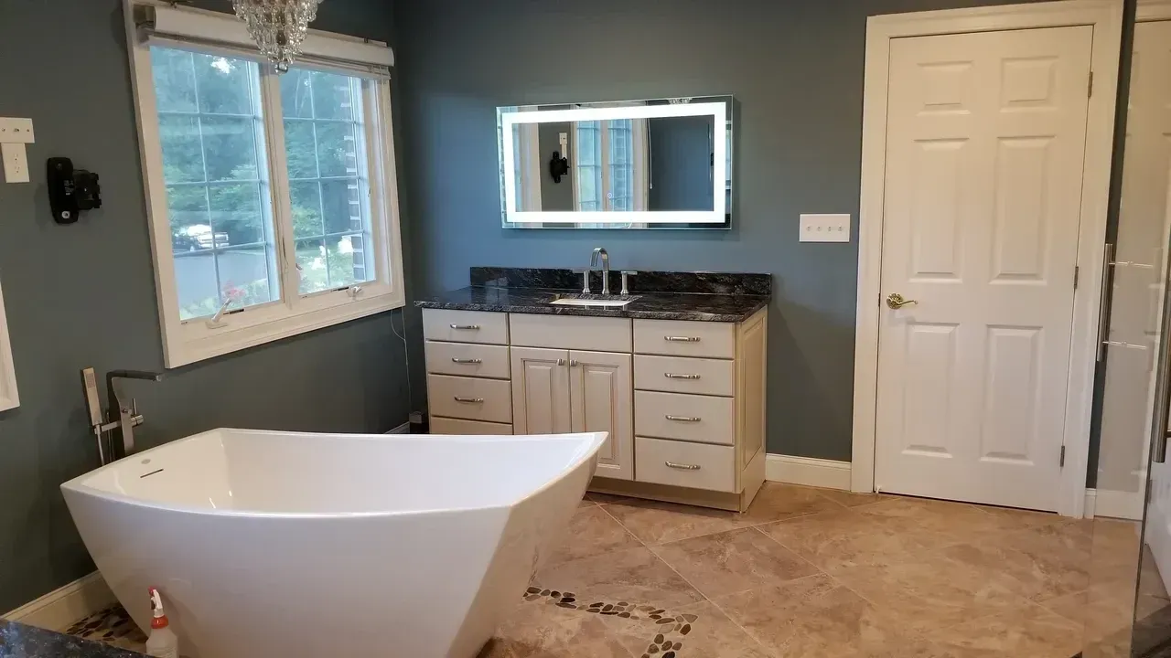 Bathroom with a white tub, vanity, and a large mirror with a built-in light, blue walls, and tiled floor.