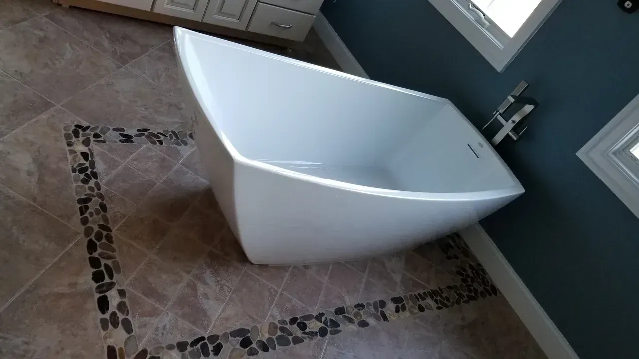 White bathtub in a modern bathroom with brown tile floor and dark stone border. Blue wall with white window frames.