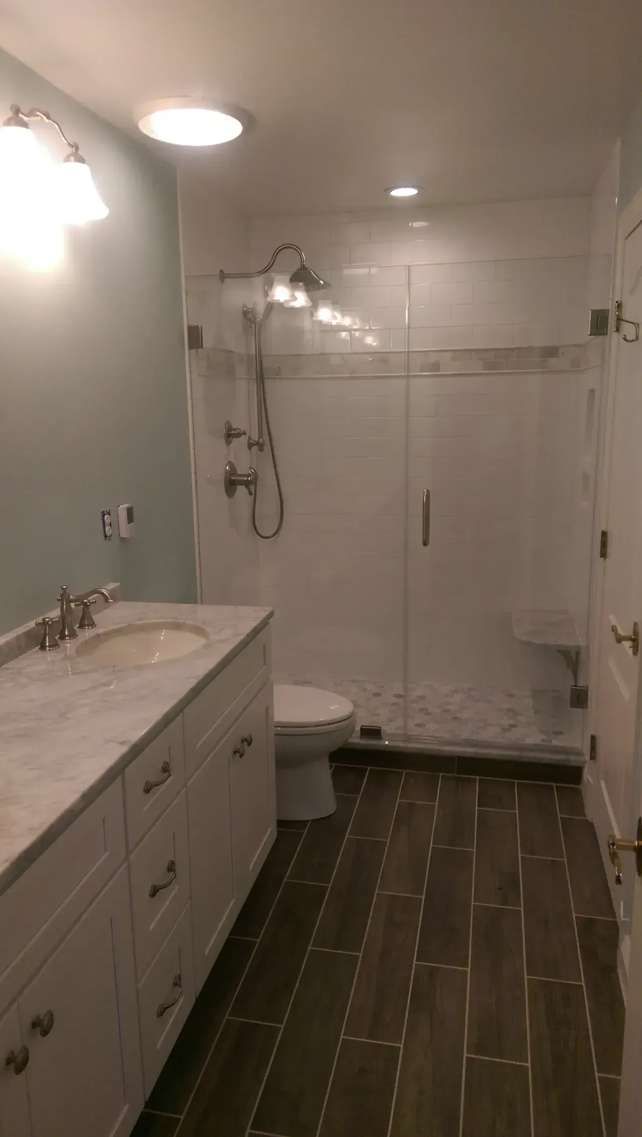 Bathroom with white cabinets, marble countertop, glass shower, and dark wood-look tile floor.
