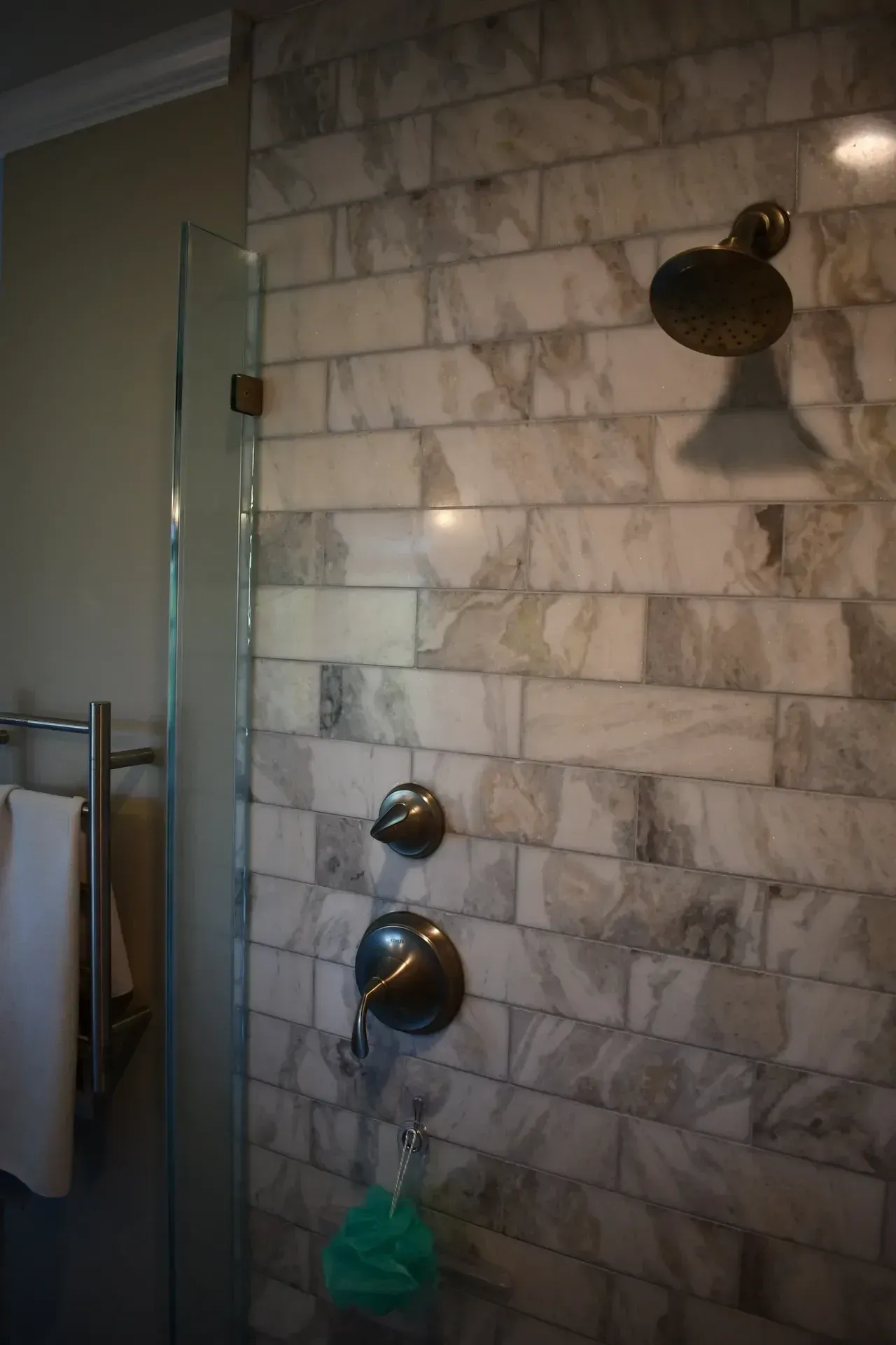 Shower with white marble brick-like tile, brass fixtures, and a glass door.