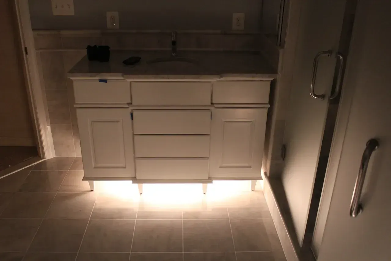 White bathroom vanity with three drawers and under-cabinet lighting.
