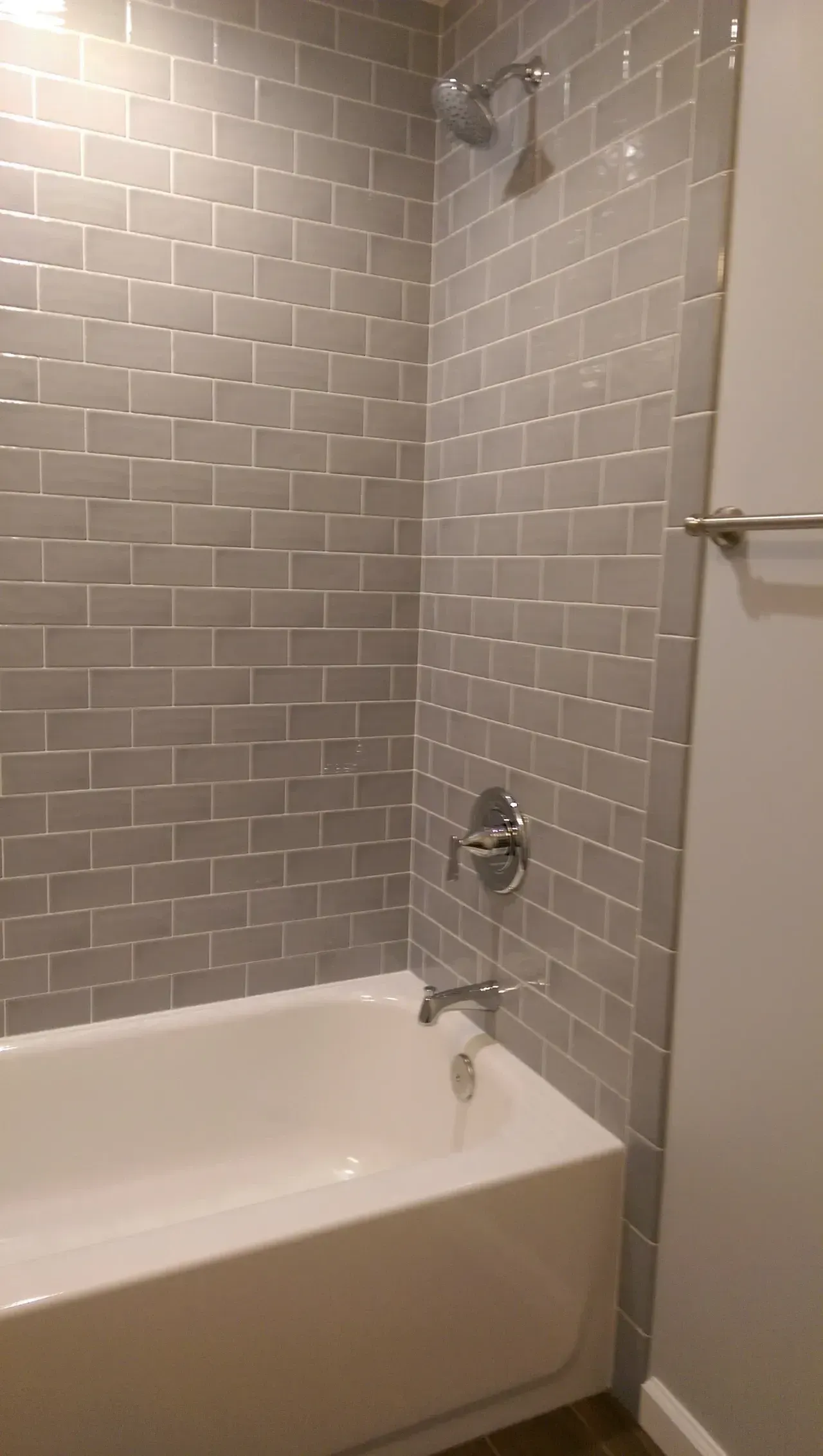 Gray tiled shower with white bathtub and chrome fixtures.