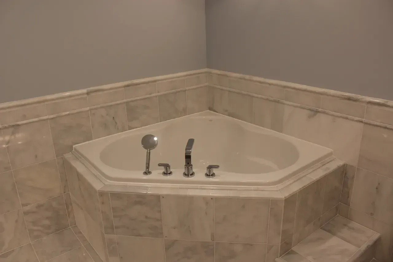 Corner jacuzzi tub in a bathroom, surrounded by marble tile and light blue walls.