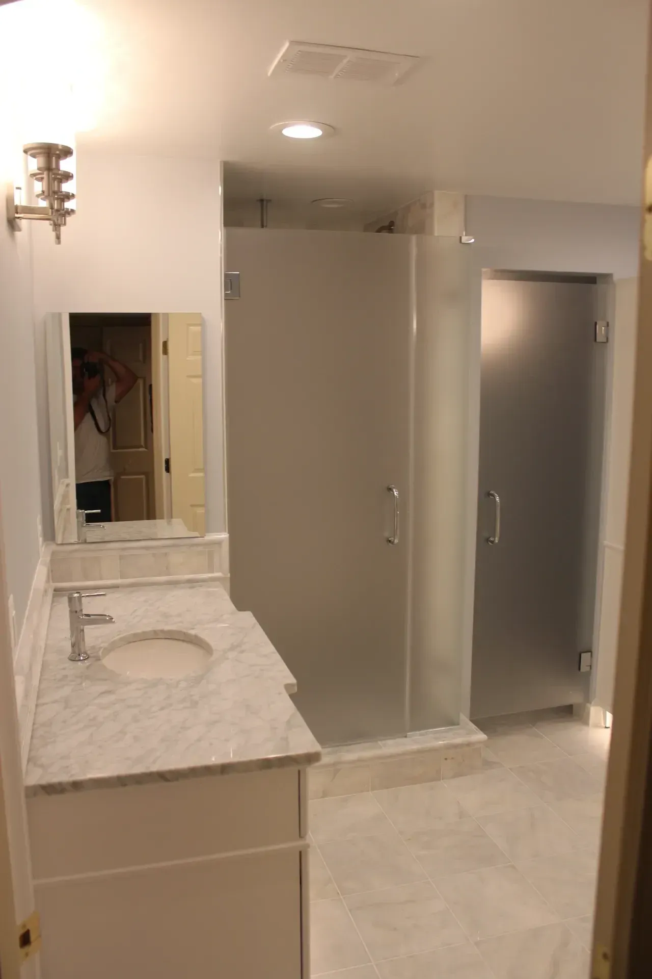 Bathroom with frosted glass shower stalls, marble countertop, and white vanity.