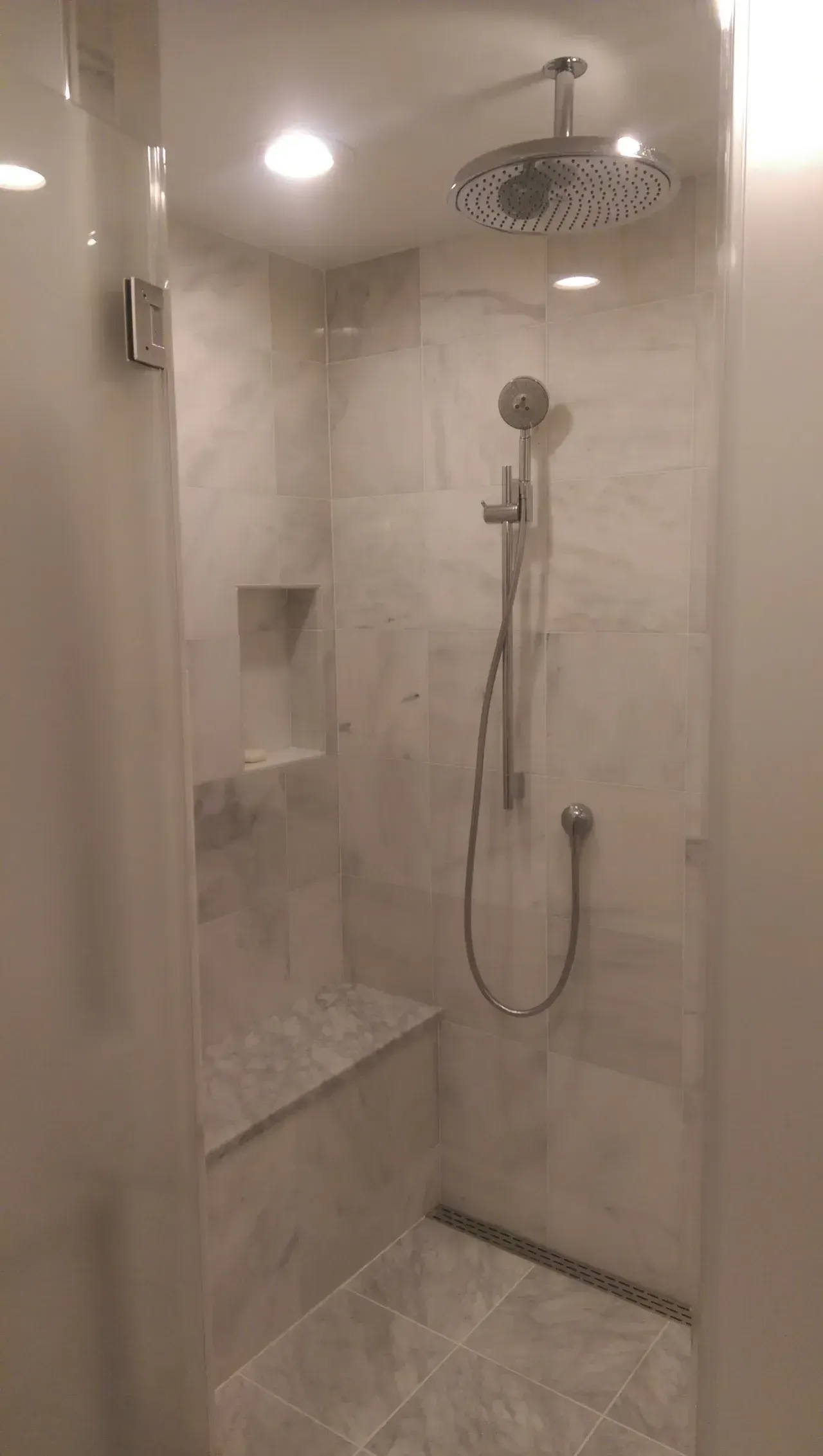 Shower with gray marble tile, glass door, built-in bench, and rain showerhead.