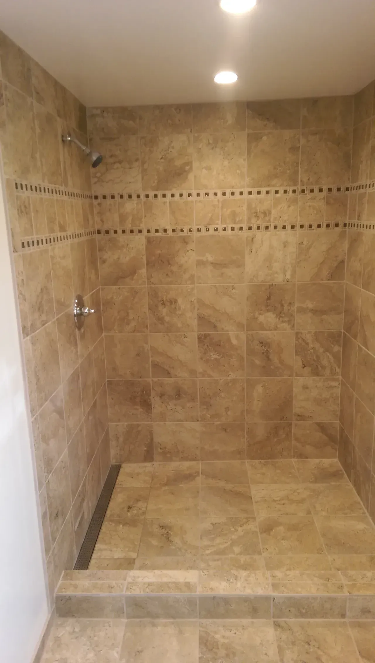 Shower with beige tile walls, mosaic accent, and step-up entry.