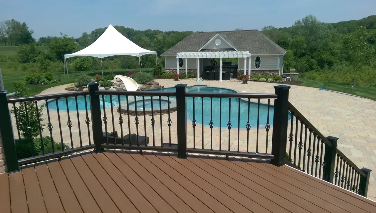 Deck overlooking pool, spa, gazebo, and tent in a sunny outdoor setting with trees in the background.