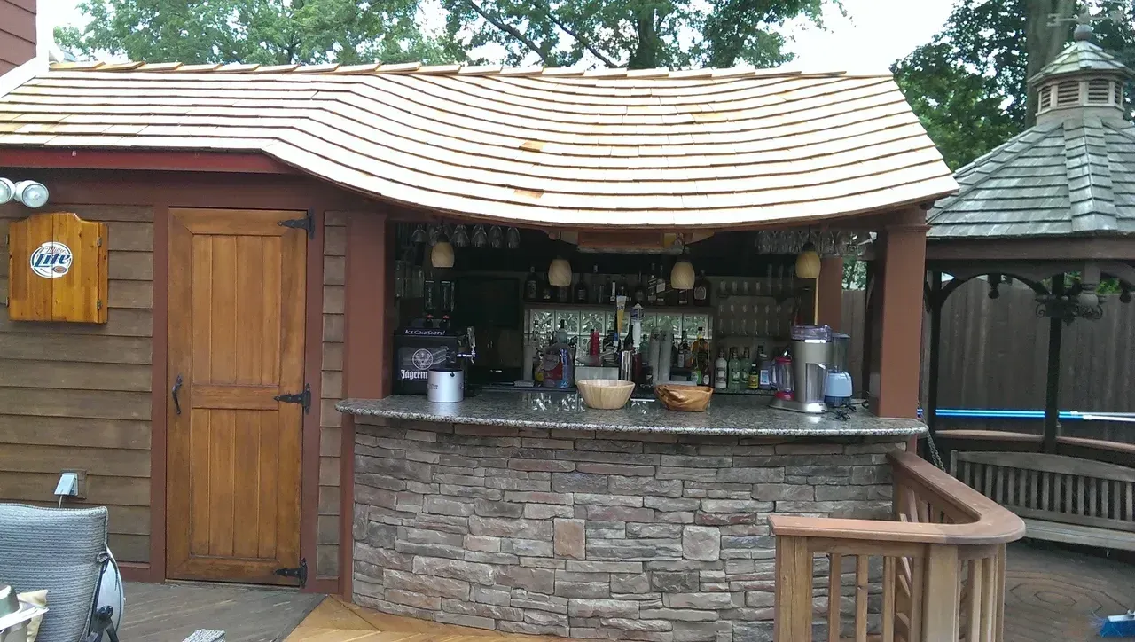 Outdoor bar with stone facade and wood roof, bottles and glasses behind the counter.