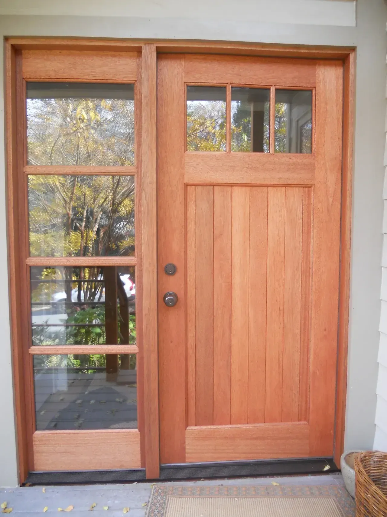 Wooden Craftsman-style front door with sidelight and transom window; warm tones.