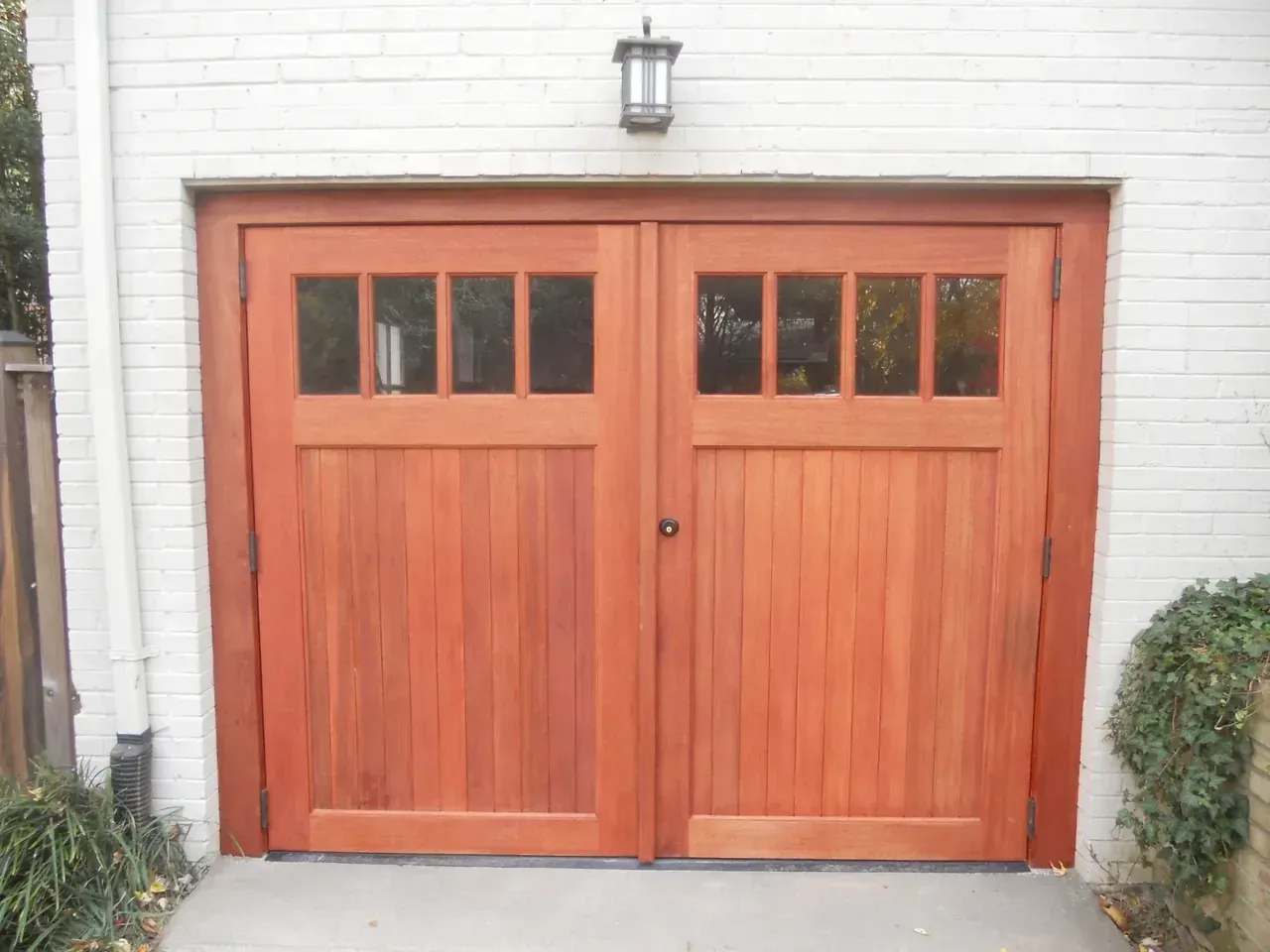 Wooden garage doors with glass panels; light fixture on a brick wall.