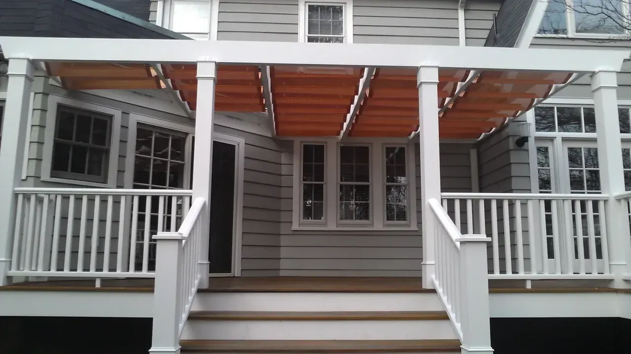 White porch with orange retractable awning, wooden steps, and house with gray siding and windows.