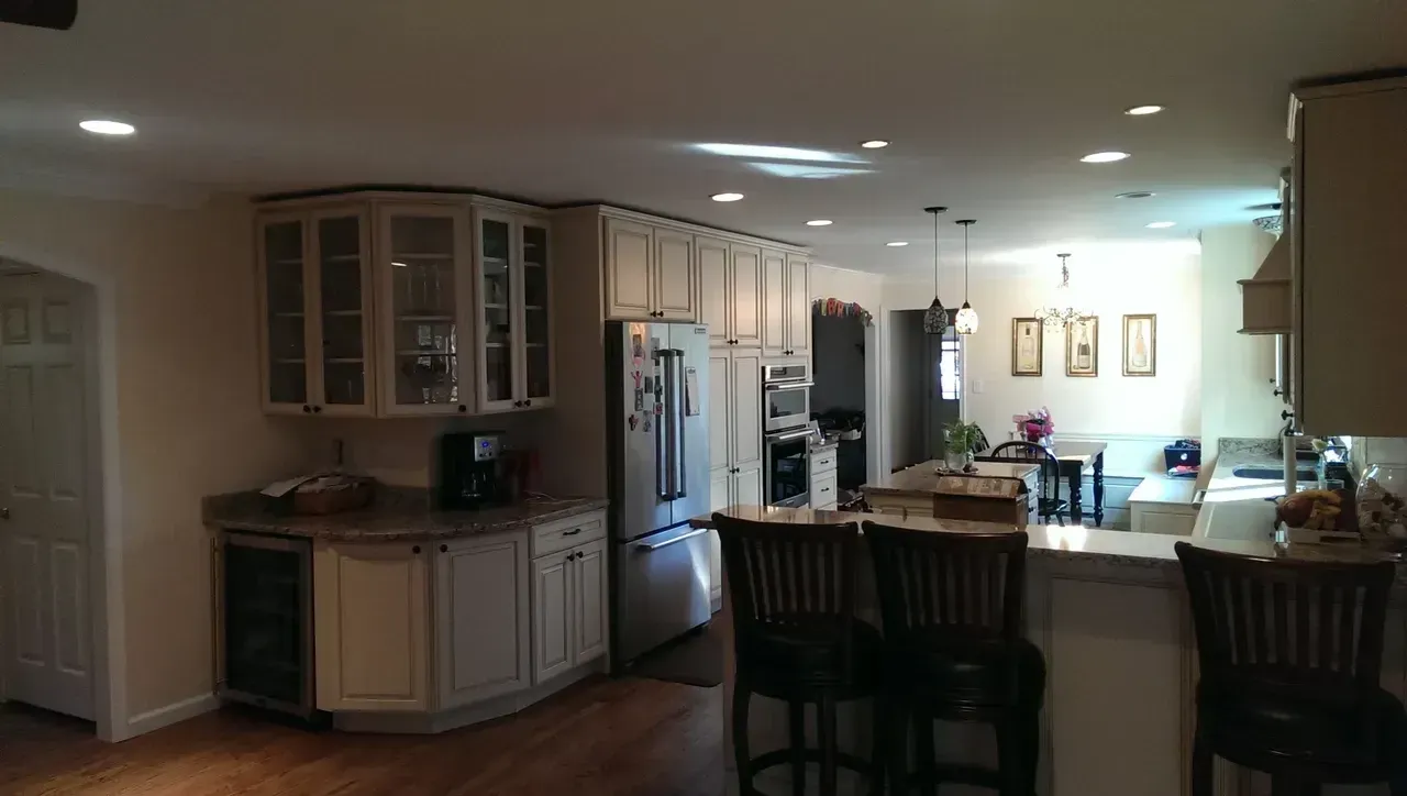 Spacious kitchen with light cabinets, stainless steel appliances, a bar with stools, and a wooden floor.