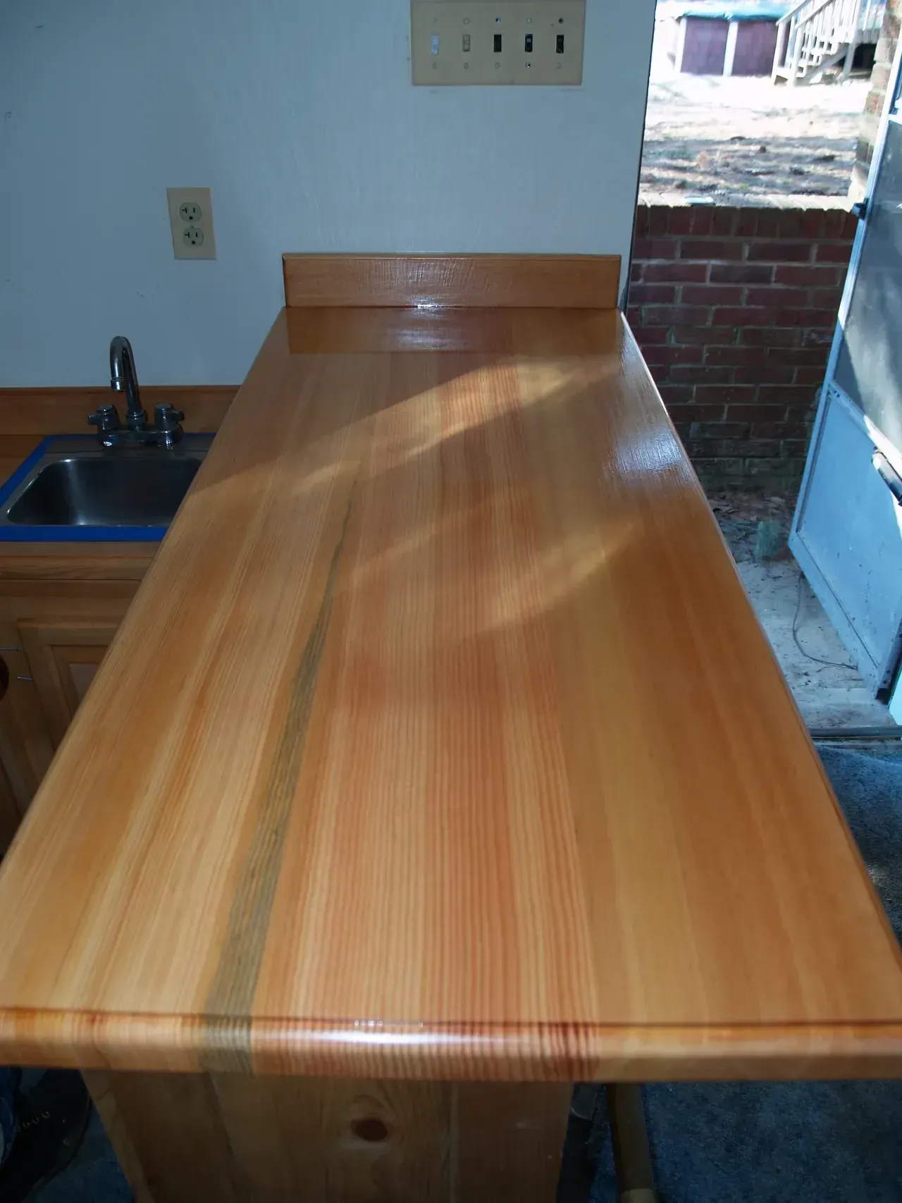 Wooden countertop with sink and light-colored cabinets, set against a white wall and brick background.
