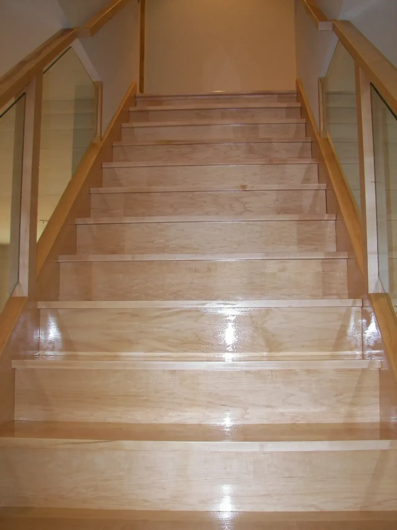 Wooden staircase with glass railing, ascending upward.