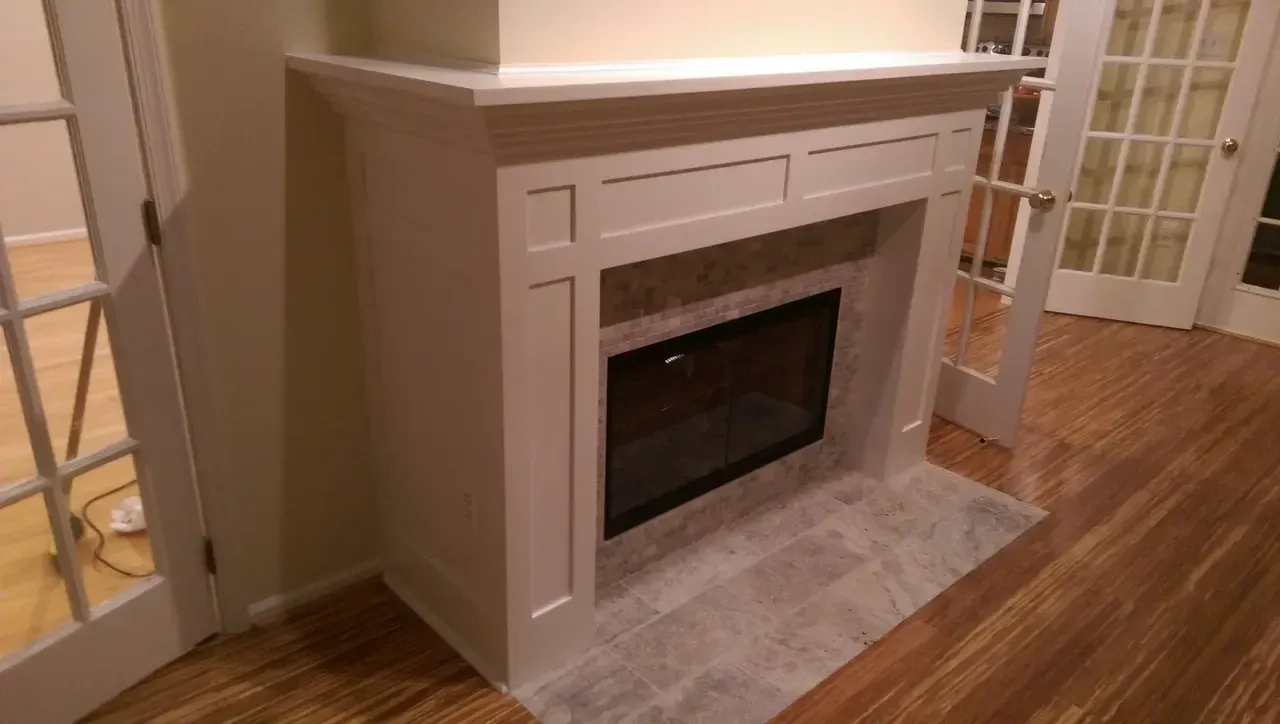 White fireplace with gray tile surround and glass fireplace, flanked by French doors.