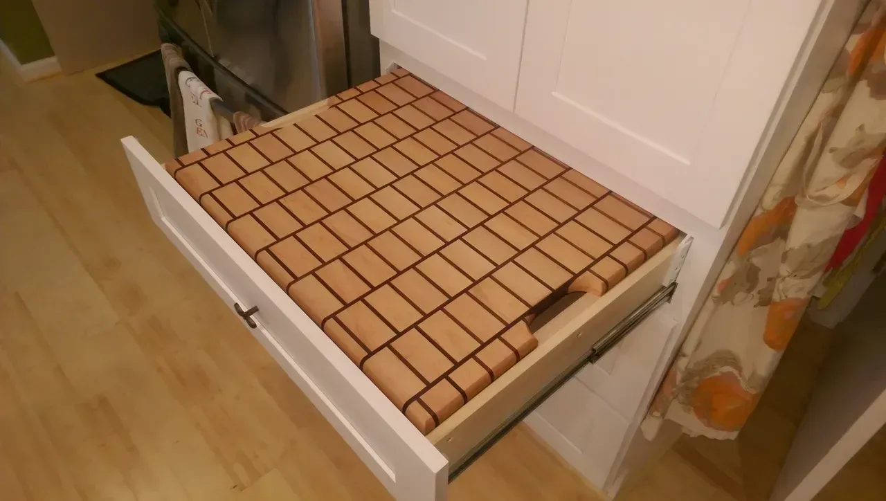 Open kitchen drawer with a bamboo-style cutting board insert.