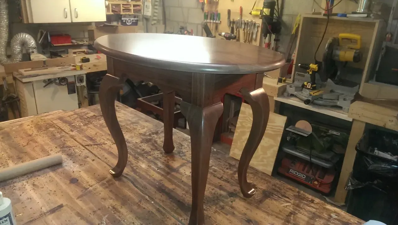 Oval-topped, dark wood table with ornate, curved legs; set in a workshop.