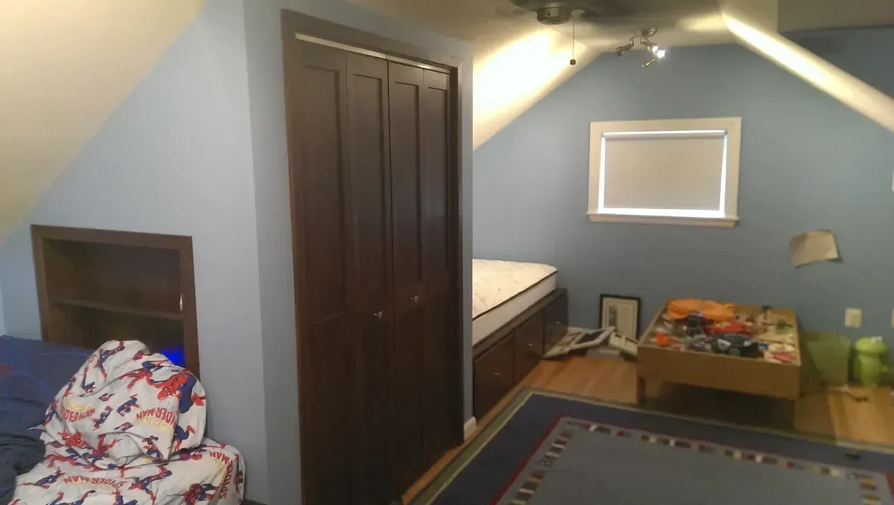 A bedroom with a bed, closet, window, and a play table. Blue walls, brown closet doors, and hardwood floors.