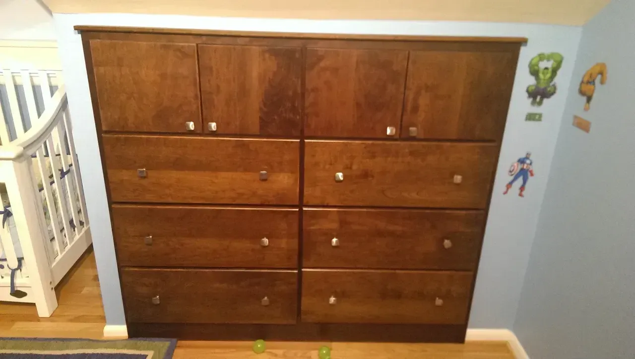 Wooden cabinet with drawers and doors in a blue-walled room; a crib is visible on the left.
